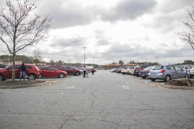 Exterior of a Walmart Supercenter behind a wide daytime parking lot filled with cars.