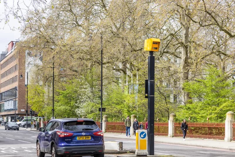 A Flock Safety automated license plate reader camera mounted on a metal pole beside a roadway.