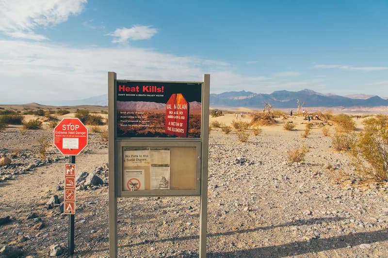 A park signboard headed Extreme Heat Warning beside a desert road under a bright sky.