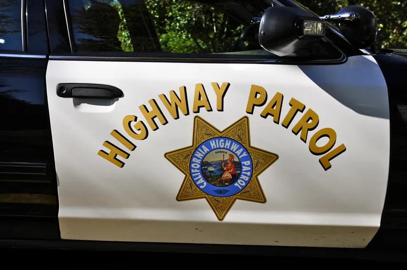 An aerial view of an overturned tractor-trailer lying across closed highway lanes, with emergency vehicles alongside and traffic backed up