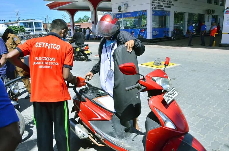 Motorbikes and three-wheelers lined up at a fuel station under a rationing notice