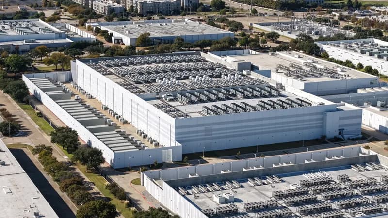 A large windowless data center building surrounded by electrical transmission equipment