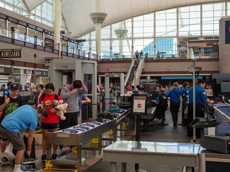 Family members greet an arriving traveler with a hug just beyond an airport security checkpoint inside a terminal.